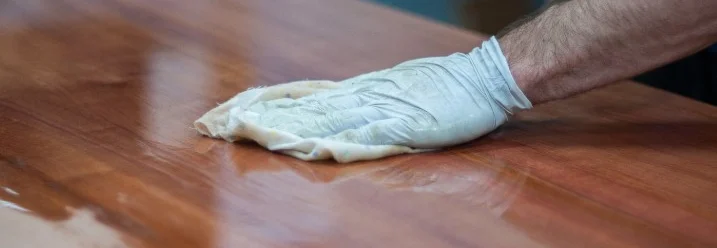 Person ölt eine Holzplatte mit einem Lappen.